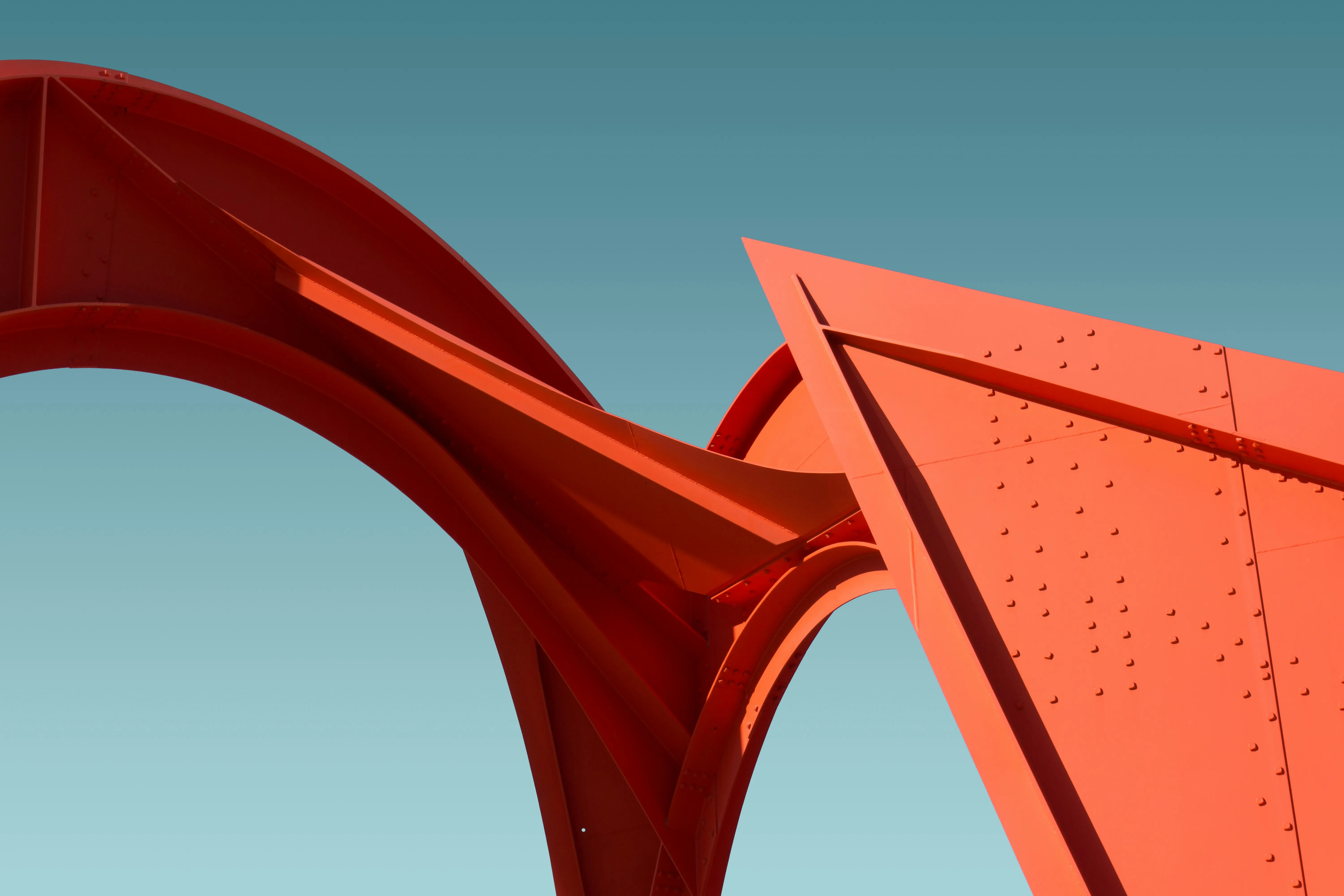 Close-up of bright orange-red curved metal structure against a clear blue sky.